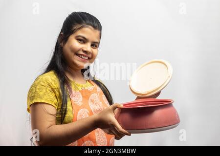 A pretty Indian housewife woman in cooking apron with opening serving casserole on white background Stock Photo