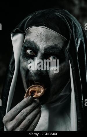 closeup of a scary evil nun eating a human finger with her bloody teeth, wearing a typical black and white habit Stock Photo