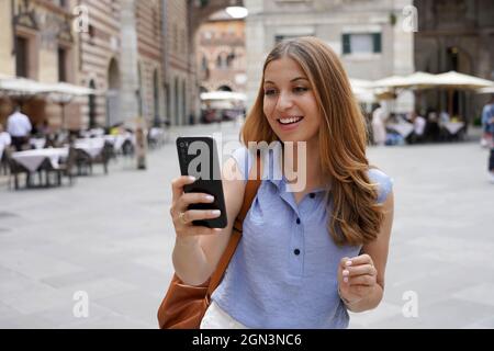 Video Call. Transfer student using phone for internet call in city street. Beautiful student girl video calling with smartphone outdoors. Stock Photo