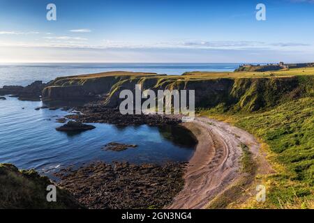 The cliffs and beach at Strathlethan Bay, near Stonehaven in Aberdeenshire, with Dunnottar Castle in the distance. Taken just after sunrise. Stock Photo