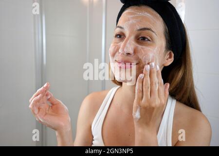 Young Skin Care Routine. Girl washing face foaming soap scrubbing skin. Face wash exfoliation scrub soap woman washing scrubbing with skincare cleansi Stock Photo