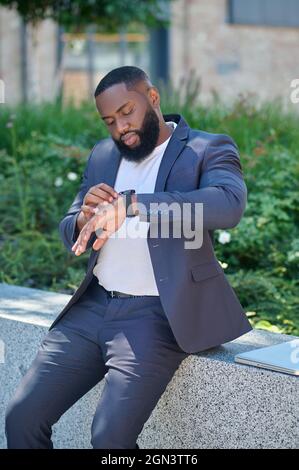A dark-skinned man in a suit looking at the watch Stock Photo