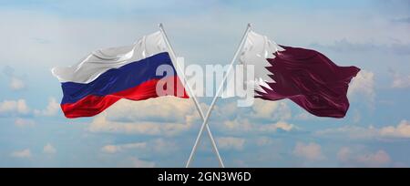 flags of Russia and Qatar waving in the wind on flagpoles against sky with clouds on sunny day. Symbolizing relationship, dialog between two countries Stock Photo