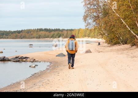 Back view of man in yellow jacket walking along lake - Image Stock Photo