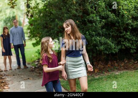 A family of a mother and father and two daughters taking a walk in the neighborhood on the sidewalk outside in the summer Stock Photo