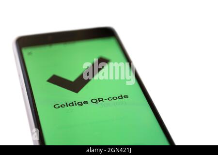Dutch text 'Valid QR code' on the green screen of a smartphone which means that the visitor has been vaccinated or tested negative. Isolated on white Stock Photo