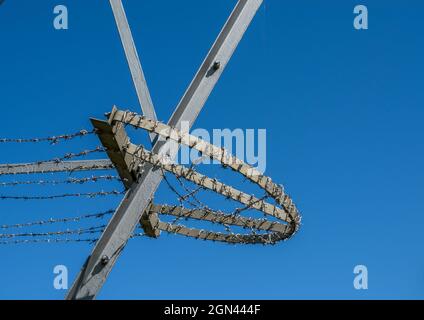 An anti climbing measure with barbed wire on a grey pylon with blue sky background Stock Photo