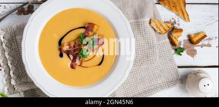 Potato soup cream with bacon and soy sauce in white bowl, on light old wooden background. Top view. Stock Photo