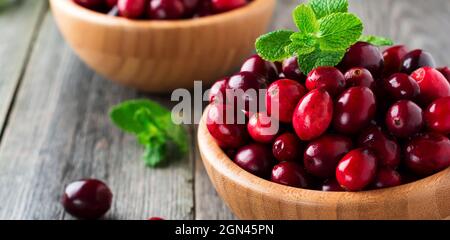 Fresh juicy cranberries in a bamboo bowl on the old wooden background. Selective focus. Stock Photo