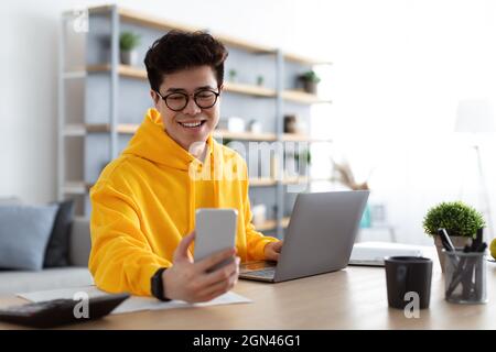 Happy asian man sitting at desk reading text message Stock Photo