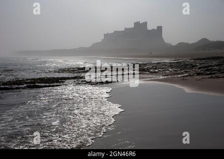 Waves breaking at Bamburgh Beach looking towards Bamburgh Castle on a misty morning, Northumberland, UK, Stock Photo