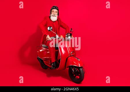 Photo of confident cute age gentleman wear new year costume headwear riding motorcycle smiling isolated red color background Stock Photo