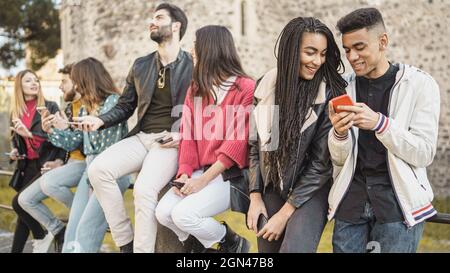 young friends watching viral social media video on mobile cell phone outdoors - Young adult friends using smartphones together -outdoors youth culture Stock Photo