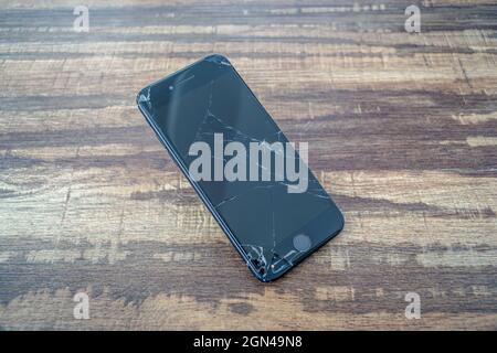 PARIS, FRANCE - Sep 12, 2021: A closeup of the broken glass screen of an iPhone 7 smartphone on a wooden table Stock Photo