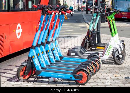 Lime and Dott e scooters for hire in London, UK, with London buses. Electric scooter rental scheme businesses, parked in busy city street Stock Photo