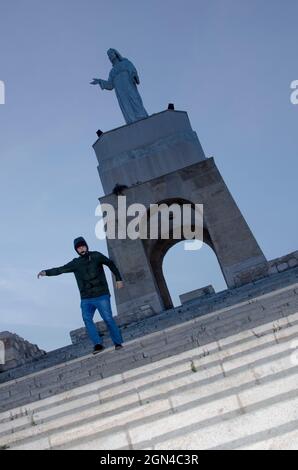 young man runs down some stairs on a hill in a city where at the top there is a statue Stock Photo