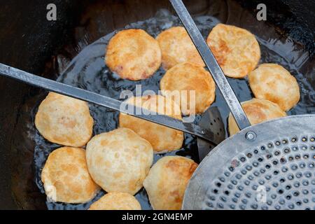 Kochuris are being fried in a frying pan. Kochuri, kachori of kachauri is a spicy snack, fried dumpling and a very popular street food in India. Stock Photo