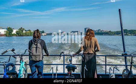 Rotterdam Netherlands - August 22 2021; Passenger ferry crossing Rotterdam harbor with two women standing at stern watching the city skyline behind. Stock Photo