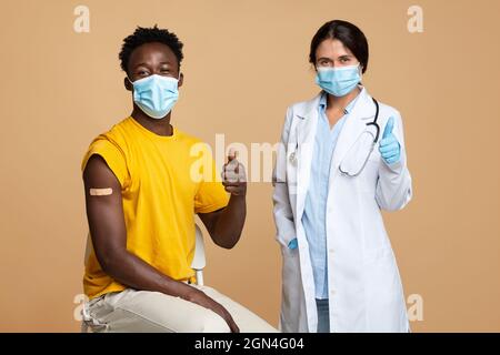 Doctor And Black Male Patient Showing Thumbs Up After Successful Vaccination Stock Photo