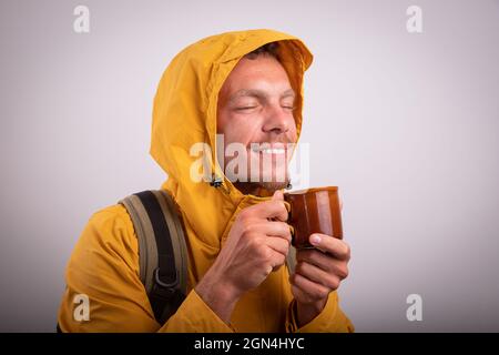 A man dressed in a waterproof jacket drinks a hot herbal tea in a cup. Man breathes the steam that comes out of a hot cup - healthy lifestyle concept Stock Photo