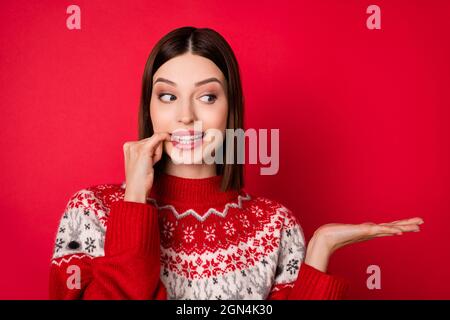 Photo of pretty cute young woman dressed print pullover finger lips holding arm looking empty space isolated red color background