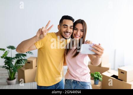 Smiling Arab guy and his Caucasian girlfriend moving to their own home together, taking selfie among carton boxes Stock Photo