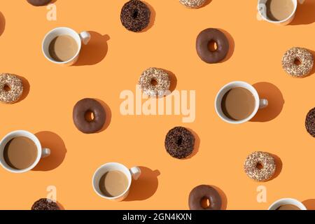 Creative food concept made of chocolate donuts, coffee in a white cup. Sweet dish pattern. Cakes and drinks on an orange background. From above. Flat Stock Photo