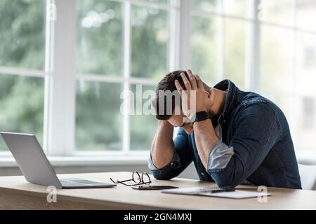 Exhausted unhappy guy touches temples to relieve pain from migraine high pressure Stock Photo