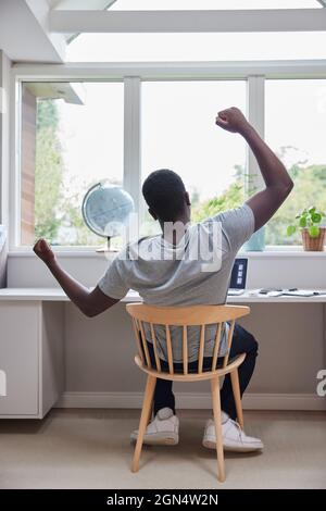Rear View Of Man Working From Home On Computer  In Home Office Stretching At Desk Stock Photo