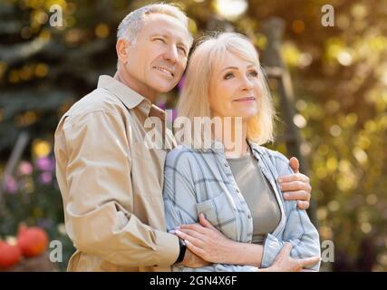 Affectionate senior spouses enjoying last warm autumn days, spending time together outdoors and looking away Stock Photo