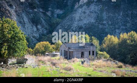 Ruins of stone house without roof and overgrown garden at the foot of a mountain. Abandoned village landscape Stock Photo