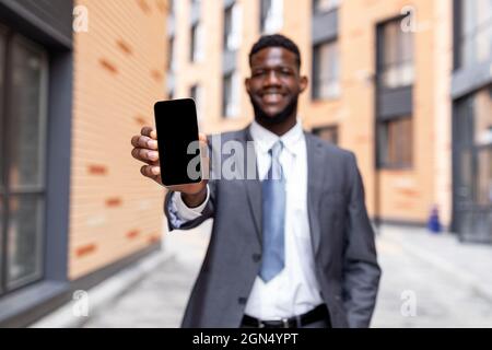 African american businessman showing smartphone with empty screen, recommending new mobile application or website Stock Photo