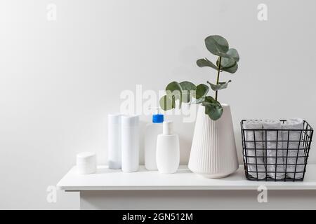Bathroom interior. Metal basket with rolled face towels, white grooved vase with eucalyptus branch, shampoo and cream jars on the shelf in the spa sal Stock Photo