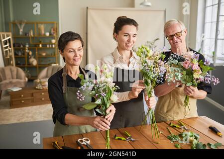 Waist up portrait of three florists arraigning flower compositions while working in cozy workshop Stock Photo