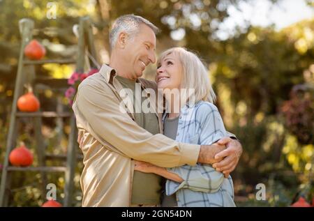 Happy loving senior spouses embracing, walking in garden and enjoying warm autumn days, spending time outdoors Stock Photo