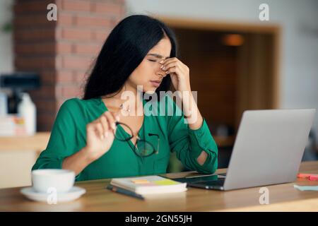 Exhausted indian lady sitting at table in front of laptop Stock Photo
