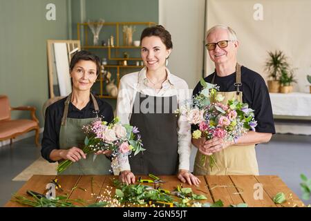 Waist up portrait of three florists arraigning flower compositions in cozy workshop and looking at camera, copy space Stock Photo