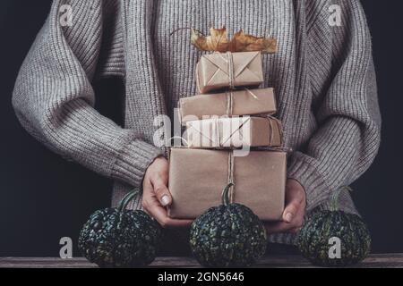 Female hands holding wrapped gifts in craft paper on a wooden table with pumpkins Stock Photo