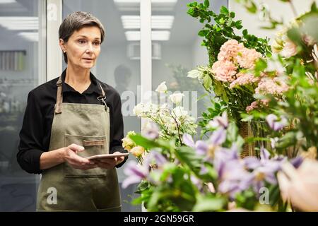 Waist up portrait of adult female florist doing stock inventory while working in flower shop, small business concept Stock Photo