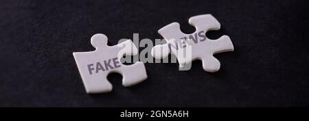 Two white puzzle pieces with fake news text on black background, close up Stock Photo