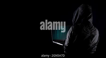 Hooded cybercriminal hacker using laptop to hack internet in cyberspace but black background, internet personal data security concept Stock Photo