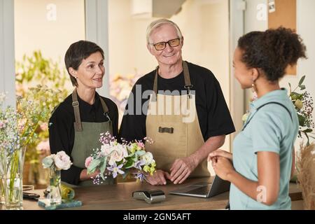 Waist up portrait of two florists talking to customer in flower shop, copy space Stock Photo