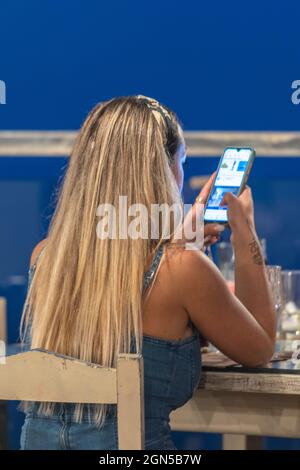 Attractive young woman using smartphone, female using mobile phone, long blond haired young woman texting, female using social media on phone. Stock Photo