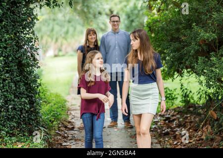 A family of a mother and father and two daughters taking a walk in the neighborhood on the sidewalk outside in the summer Stock Photo