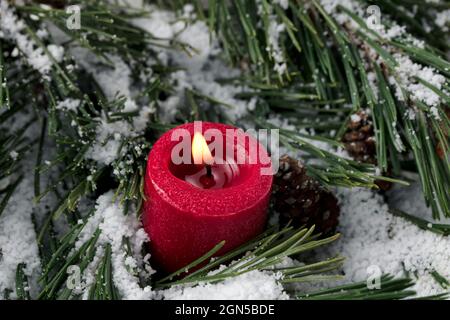 Close up view of a single burning red candle with snow covered fir tree branches in background for a merry Christmas or happy New Year holiday celebra Stock Photo