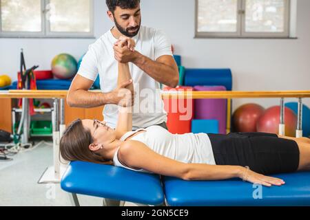 Male hysiotherapist doing elbow extension exercises with a young female patient at a clinic Stock Photo