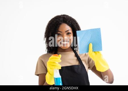 Spring cleaning african woman pointing cleaning spray bottle. Beautiful cleaning woman standing isolated on white background. Stock Photo