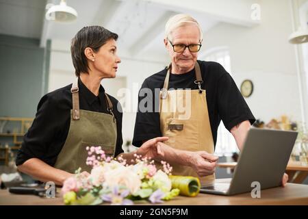 Portrait of senior business owners using laptop together while managing flower shop, copy space Stock Photo