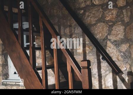 Wooden stairs with stones wall in traditional old Greek house in dark evening light with shadows Stock Photo