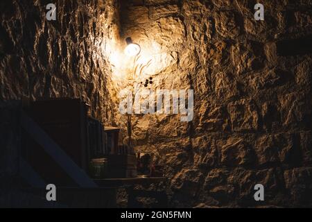Warm cozy lamp in corner on bookshelf in dark room with stone walls. Greek guest house evening rest area, decor interior elements Stock Photo
